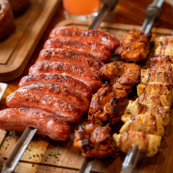 Grilled Brazilian sausages, chicken, and bacon-wrapped chicken skewers on a wooden board.