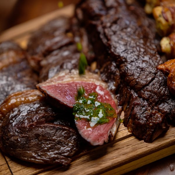 Close-up of Brazilian grilled meats, including a sliced piece with chimichurri, on a wooden board.