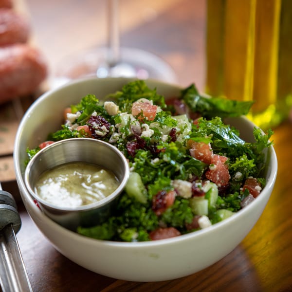 A vibrant kale salad with grapefruit, feta, and dried cranberries, served with a side of dressing.